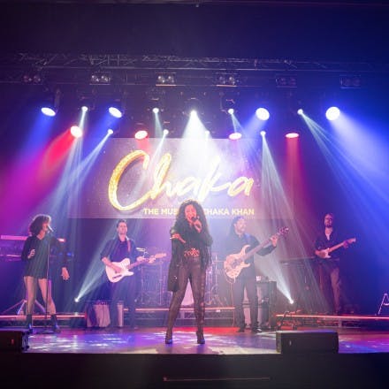 Chaka stood at the front of the stage with the band behind her covered in colourful lights.