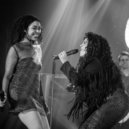 Chaka passionately singing into the mic, whilst a backing singer looks on smiling.